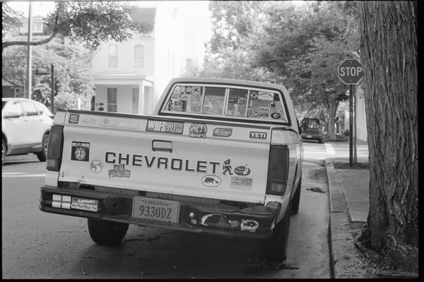 Black and white photo of a white Chevrolet truck with many stickers, including the Sex Pistols and the England flag.